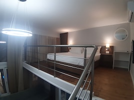 Una habitación de hotel con cama, escritorio, silla, espejo y una escalera.