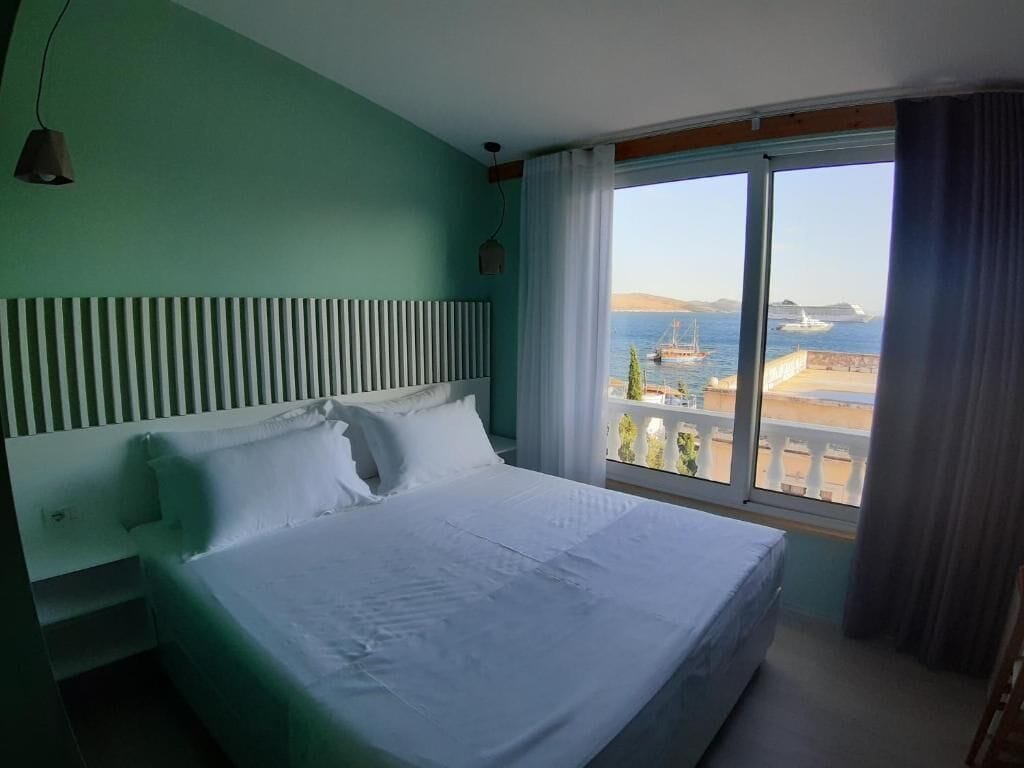 Een hotelkamer met een groot bed, uitzicht op zee en een raam met gordijnen.