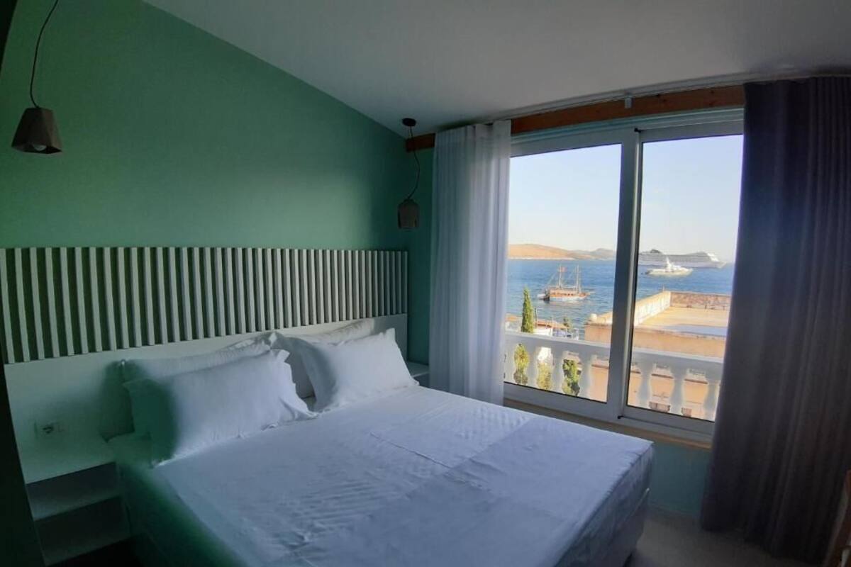 Un cuarto de hotel con una cama grande, vista al mar y una ventana con cortinas.