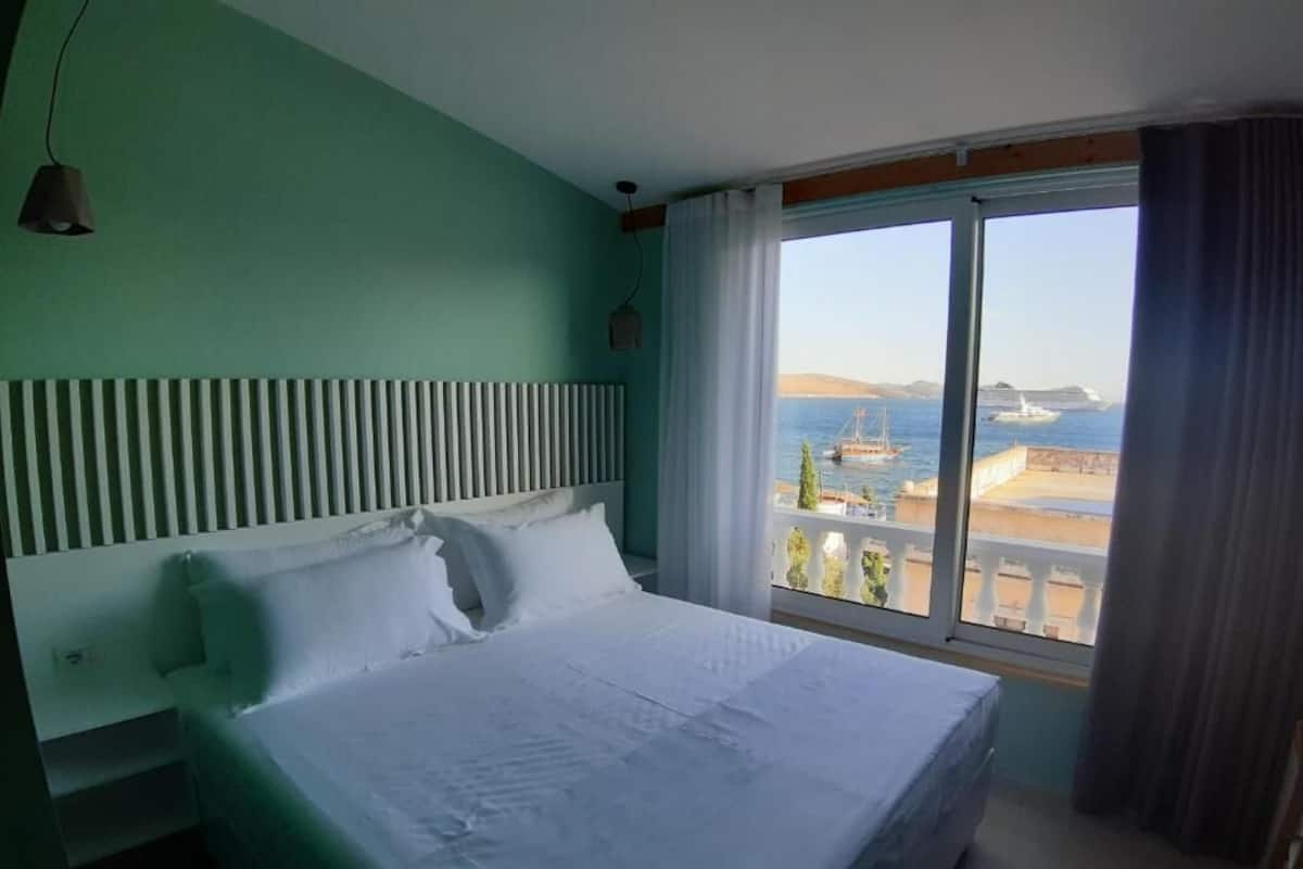 Une chambre d’hôtel avec un grand lit, une vue sur la mer et une fenêtre avec des rideaux.