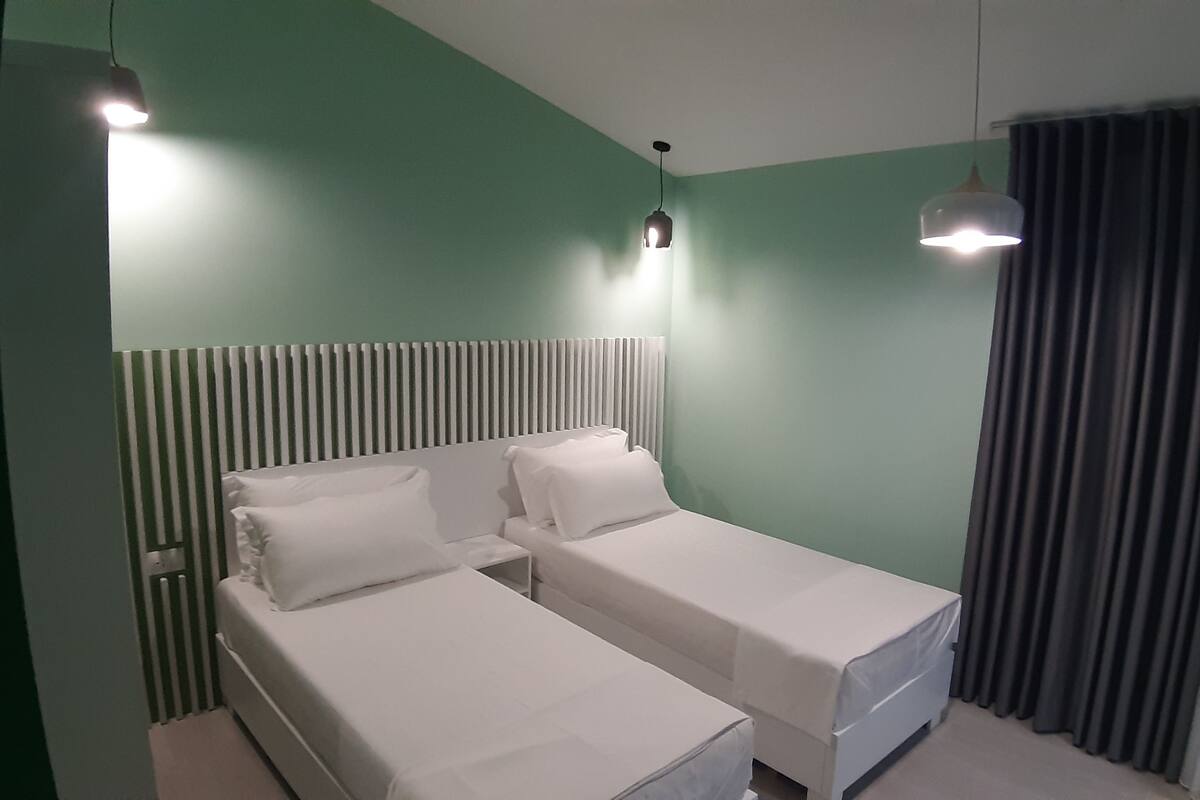 Una habitación con dos camas individuales, techo inclinado y ventana con cortinas.
