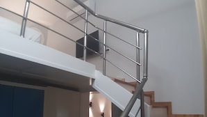 Un escalier avec des rampes en métal et des marches en bois, menant à un niveau supérieur où se trouvent une porte et un luminaire fixé au mur.