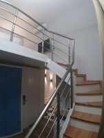 A staircase with metal railings and wooden steps, leading to an upper level with a door and a wall-mounted light fixture.