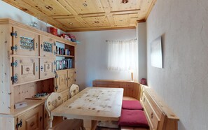 Um quarto com uma mesa de madeira, cadeiras, um banco e uma estante com livros e objetos decorativos.