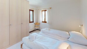 Hotellihuone, jossa on kaksi sänkyä, vaatekaappi, patteri ja tuoli.
