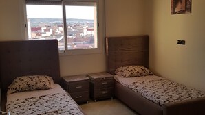 A compact room with a bed, a small table, and a window. - Appartement De Luxe 4 Chambres (Oujda)