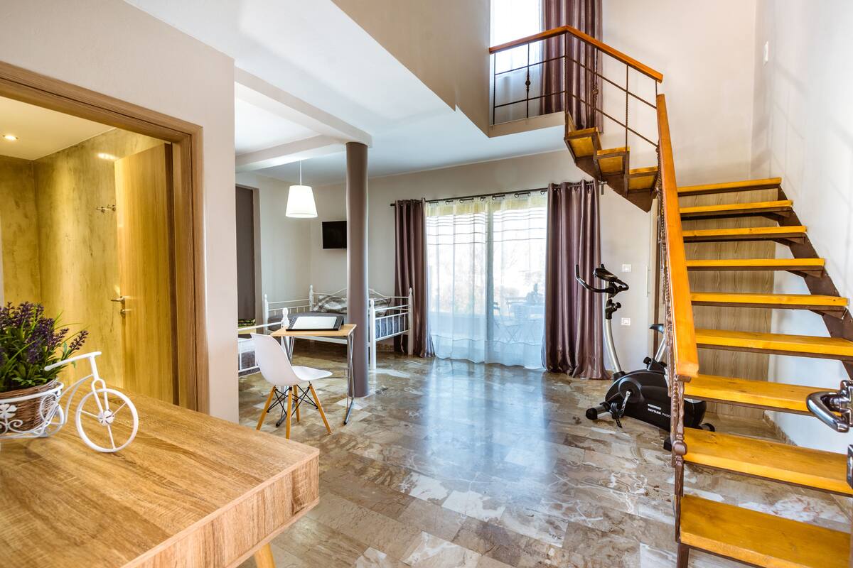 A spacious living area with a wooden staircase, a dining table with a bicycle decoration, and a home office setup.