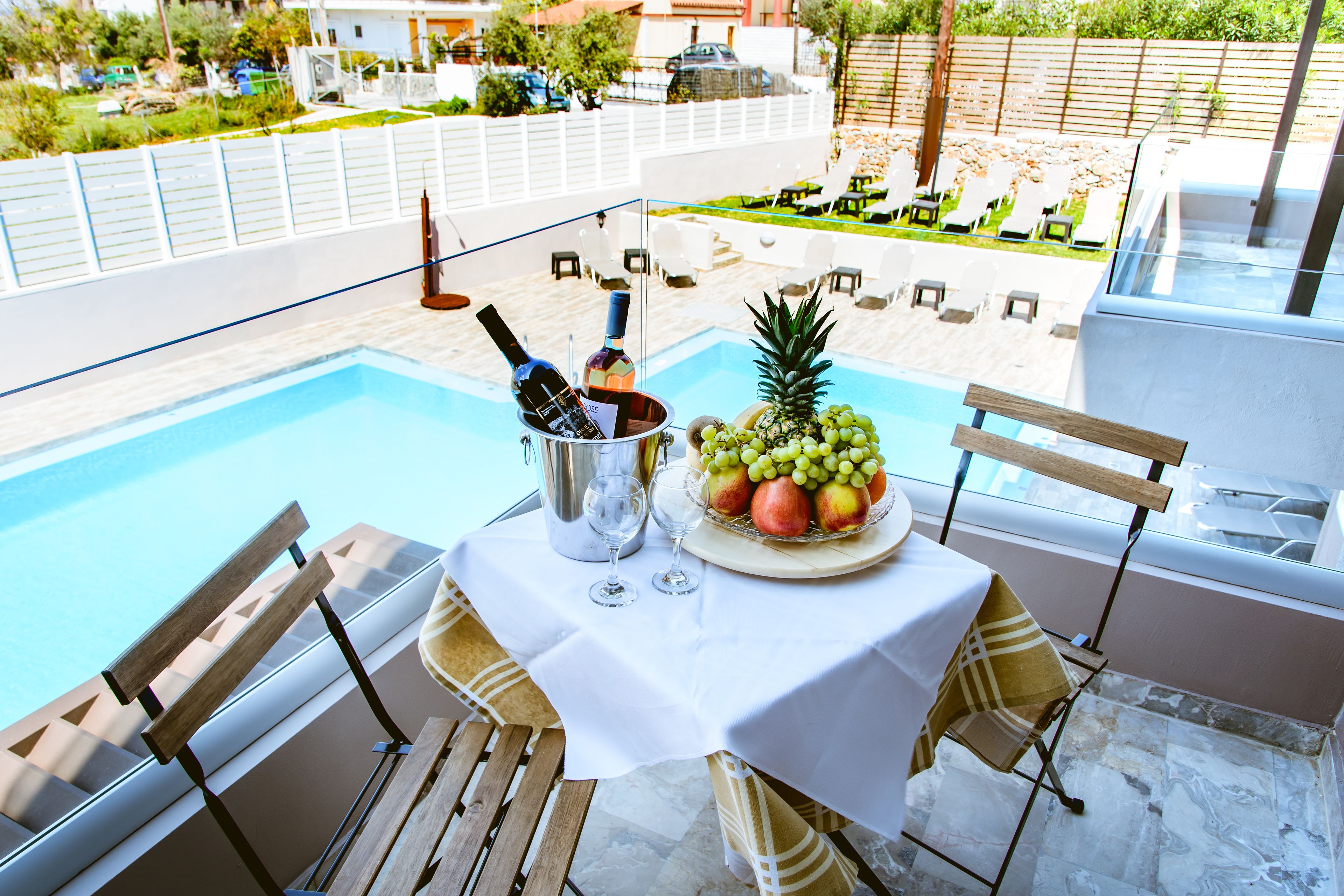 Una mesa junto a la piscina con mantel blanco, frutero y botella de vino.