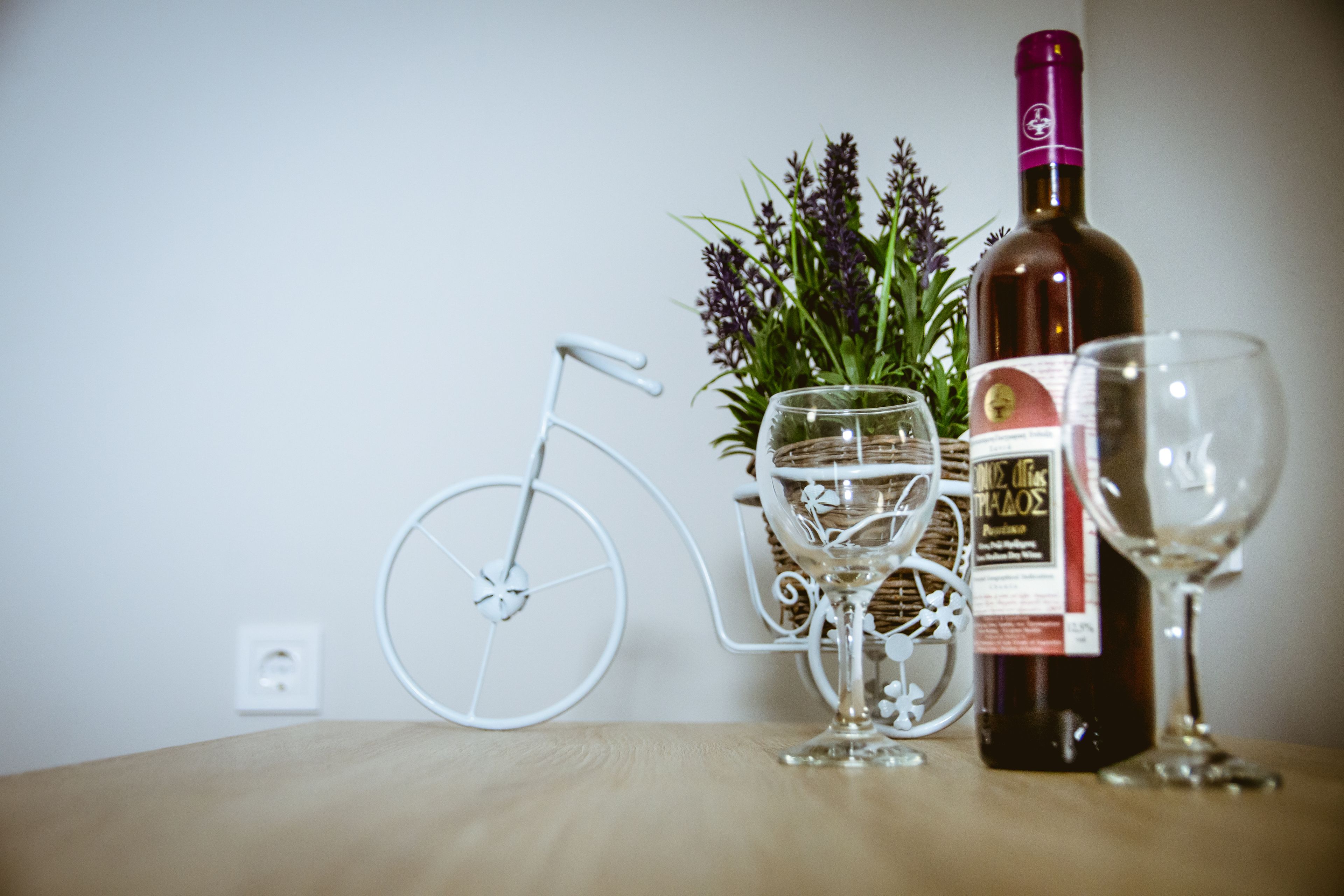 A bottle of wine, two wine glasses, and a decorative metal bicycle on a wooden table.