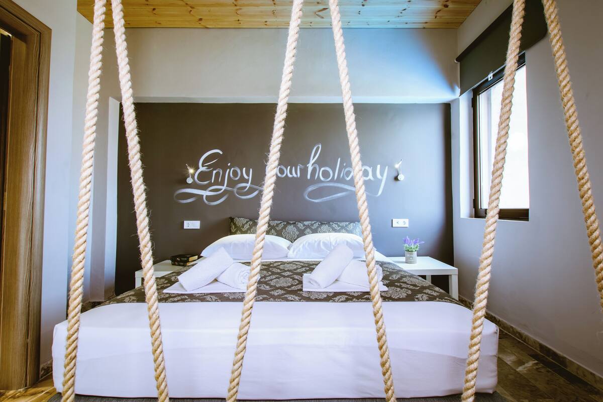 A bedroom with a bed, a bedside table, a wall with a message, and a window.