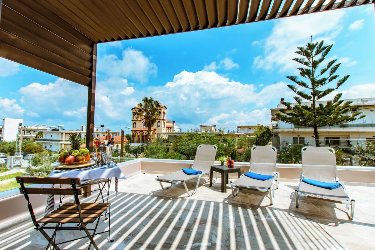 A rooftop terrace with lounge chairs and a table with fruit and drinks.
