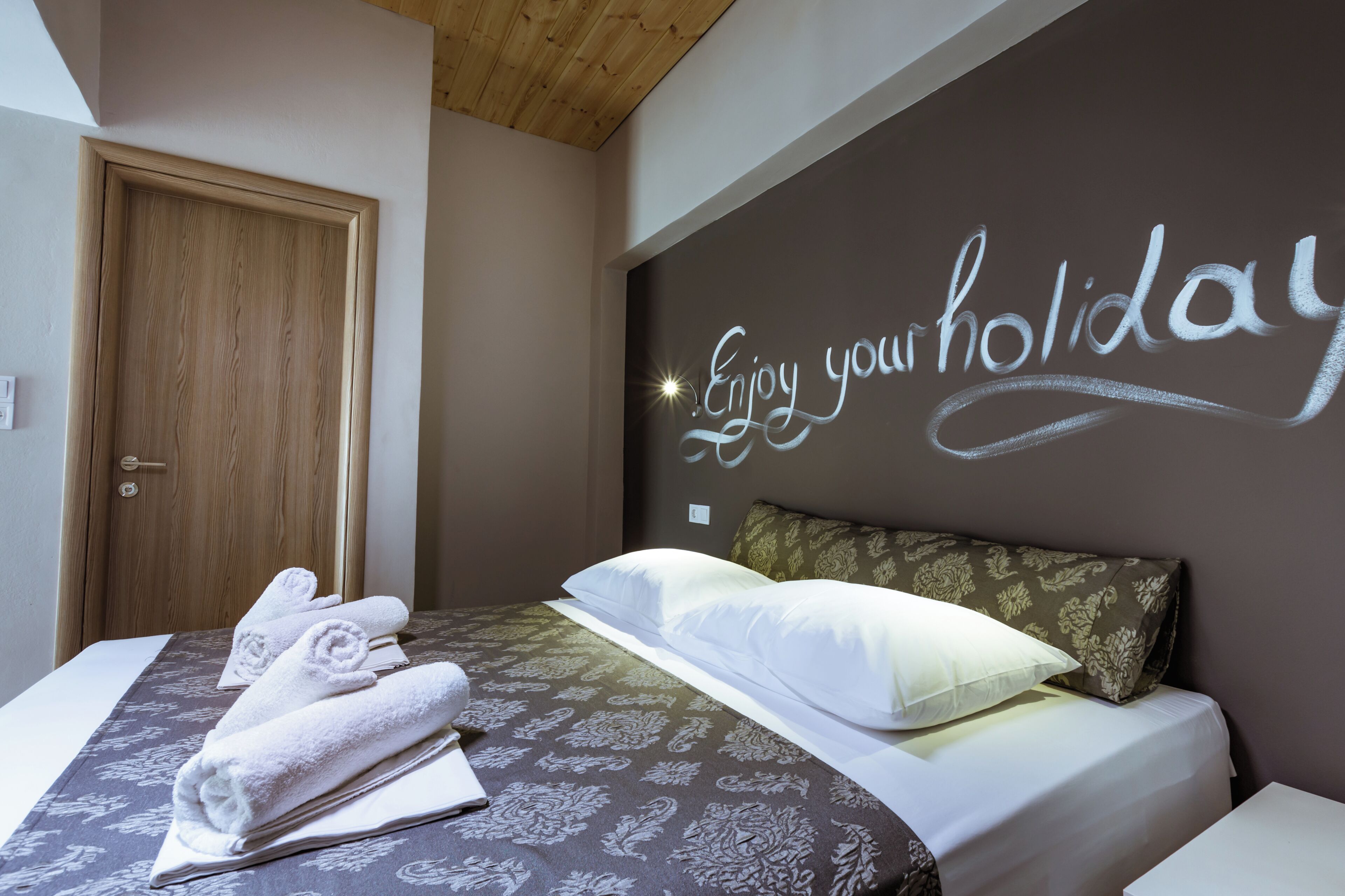 Una habitación de hotel con una cama, una pared con el letrero 'Enjoy your holiday', una puerta de madera y una cama bien hecha con toallas.