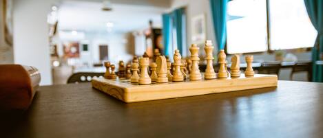 A wooden chessboard on a table in a room with a window and curtains.