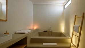 Un baño moderno con una bañera independiente, un banco de madera, un perchero y un espejo.