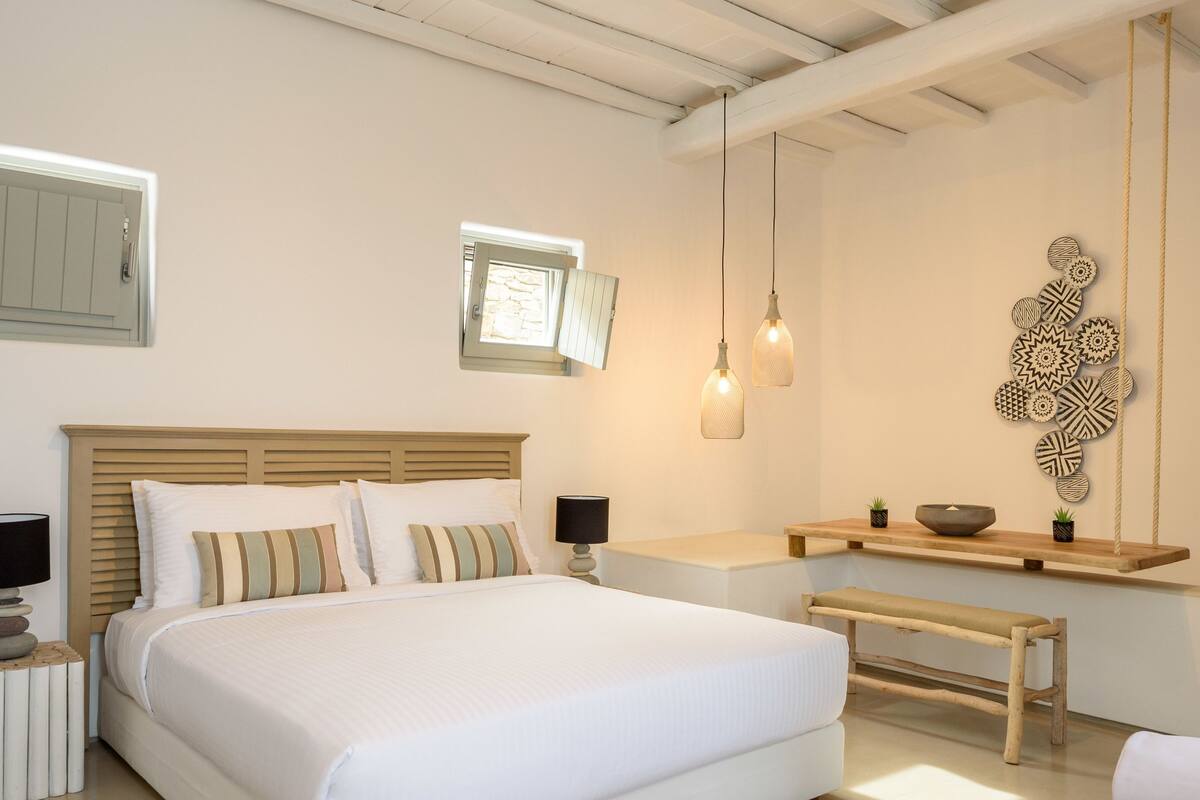 A modern bedroom with a large bed, bedside tables, a small window, and a wall-mounted decorative piece.