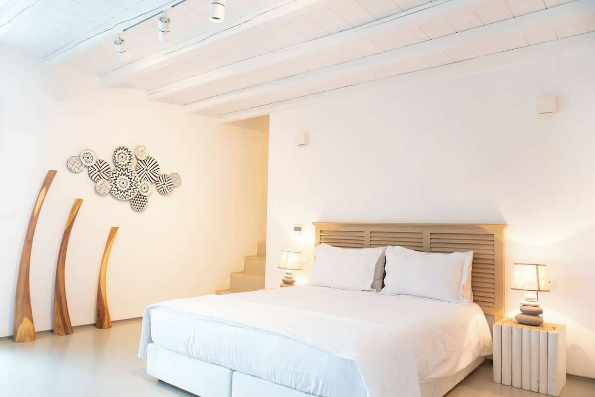 A modern bedroom with a large bed, wooden headboard, and a staircase leading to an upper level.