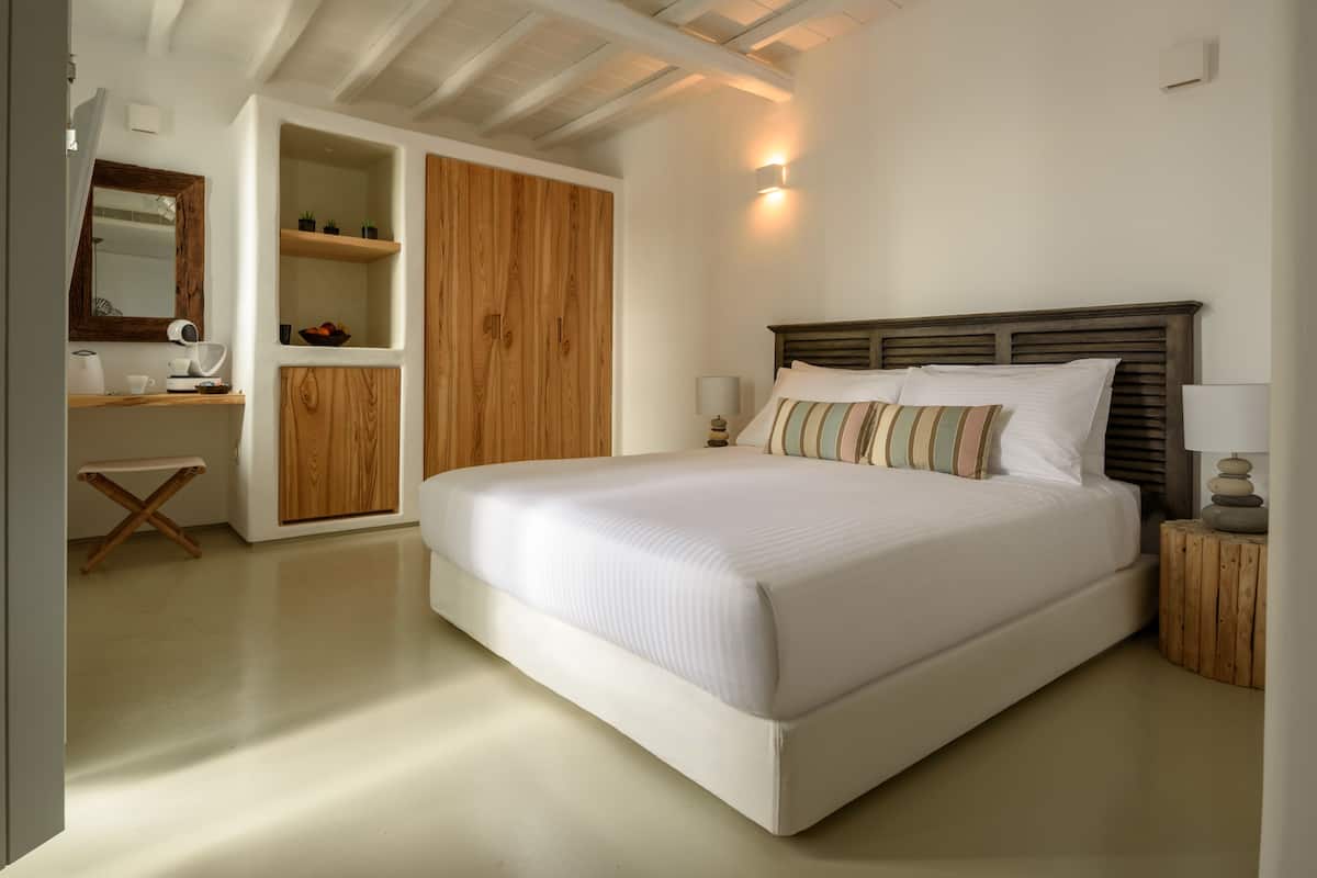 A bedroom with a large bed, wooden wardrobe, bedside tables, and a small desk with a chair.