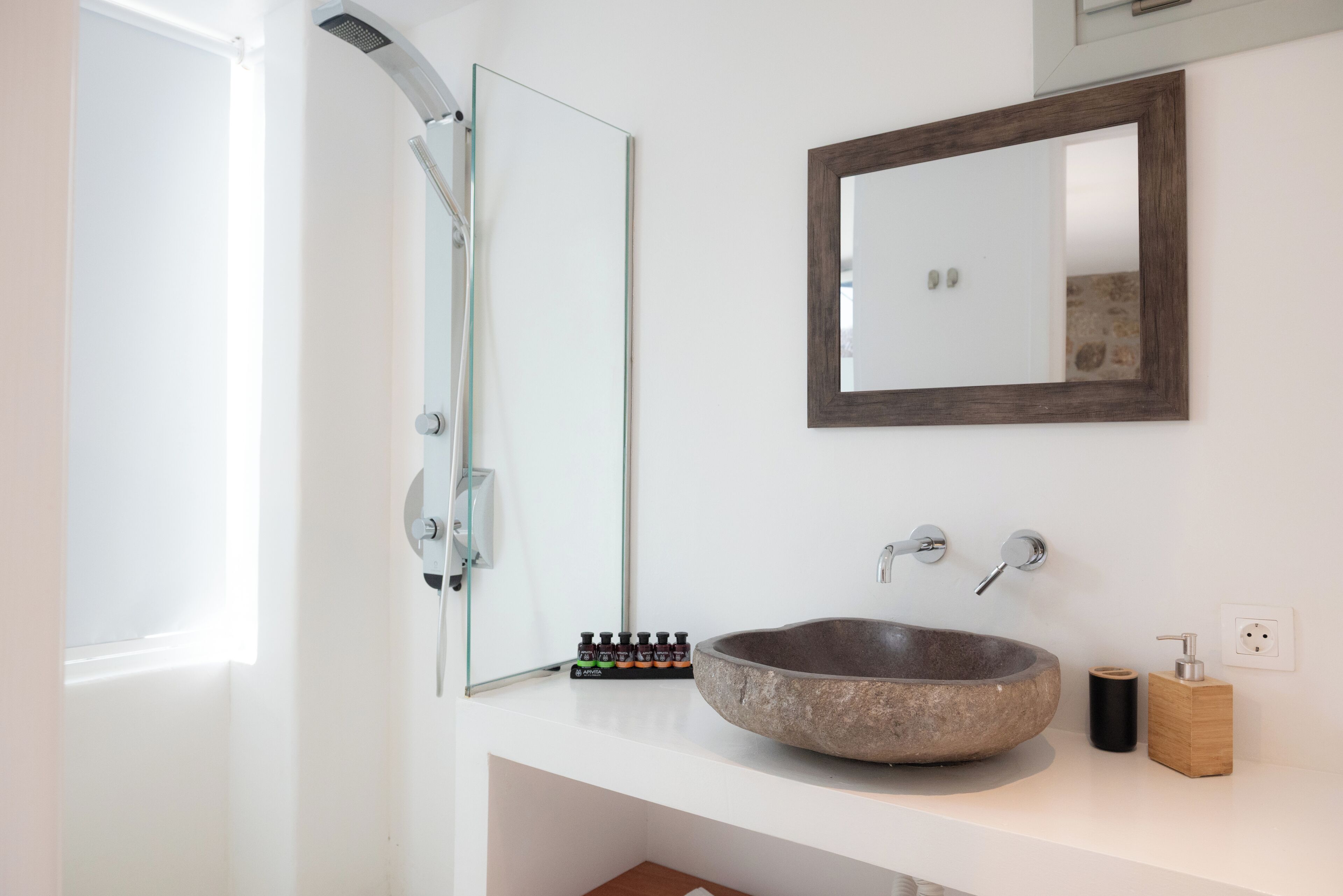 Un baño con lavamanos de piedra, un espejo grande y una ducha.
