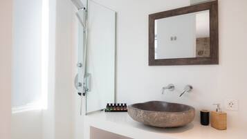 Un baño con lavamanos de piedra, un espejo grande y una ducha.