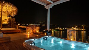 Un jacuzzi con terraza de madera y vista a la ciudad de noche.