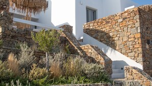 Un edificio moderno con paredes blancas y detalles de piedra, que presenta una escalera de piedra y una estructura de tejado de paja.