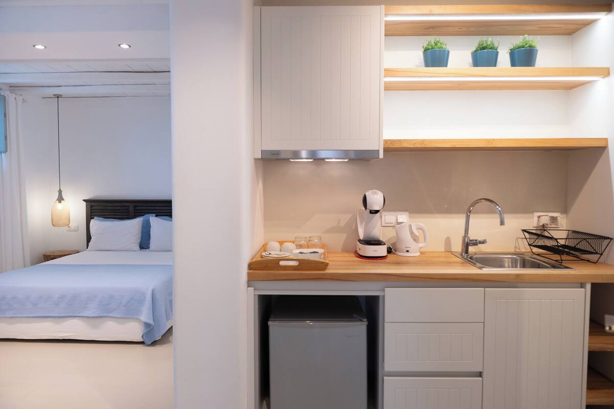 A modern hotel room with a bed, a compact kitchenette, and a small refrigerator.