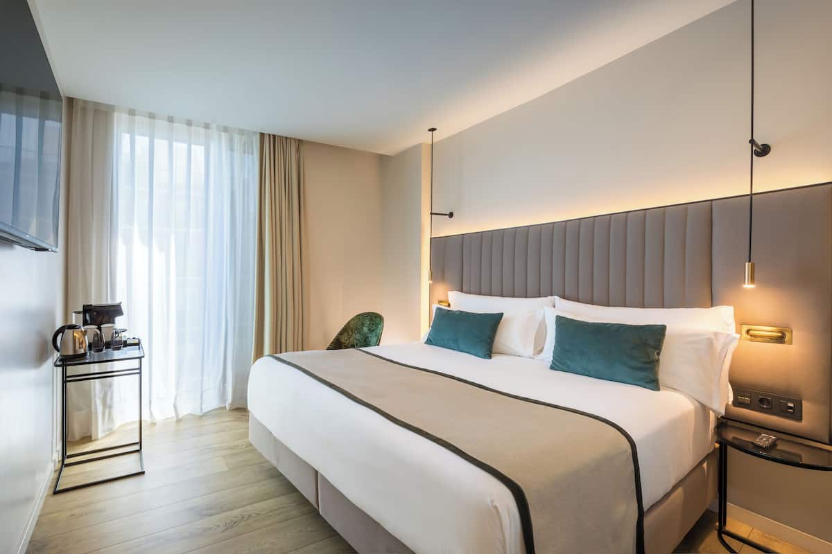 Quarto de hotel com uma cama grande, mesas de cabeceira, televisão e uma janela com cortinas.