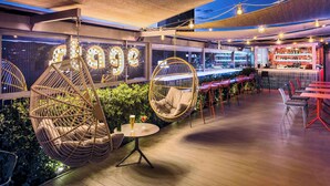 Un bar en la azotea con sillas colgantes, zona de bar y vista nocturna de la ciudad.