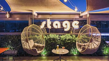 A rooftop bar with hanging chairs, a table with drinks, and a 'stage' sign.