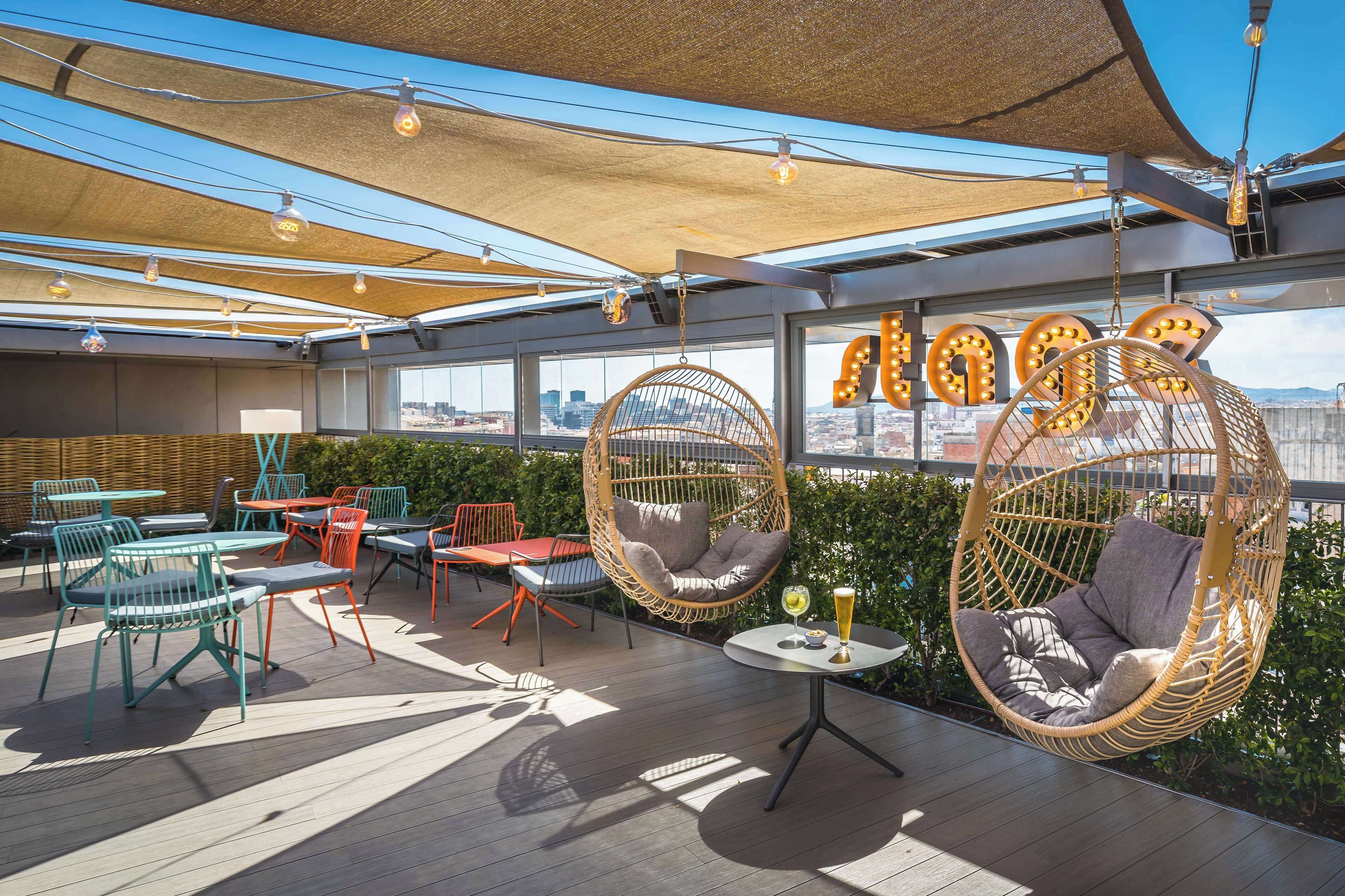 A rooftop terrace with hanging chairs, tables, and a city view.