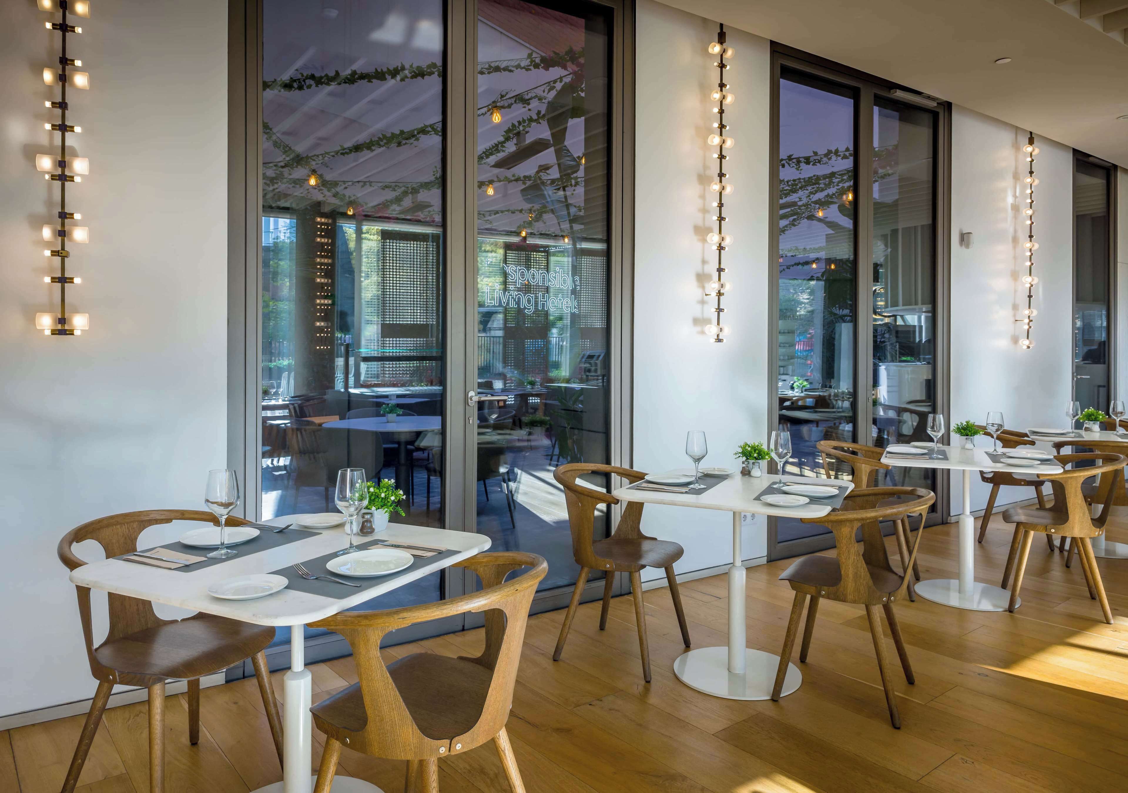 A modern restaurant with wooden chairs and tables, large windows, and string lights.