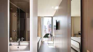 Une chambre d’hôtel moderne dotée d’une salle de bain, d’un lit, d’un bureau et d’une fenêtre donnant sur la ville.