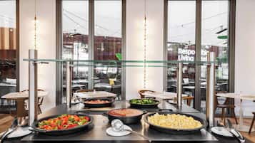 A buffet setup with various dishes, a glass partition, and a view of the outside through large windows.