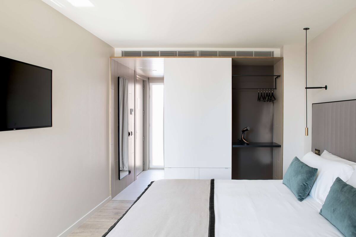 Quarto de hotel moderno com uma cama grande, televisão de tela plana na parede, closet espaçoso e área de chuveiro.