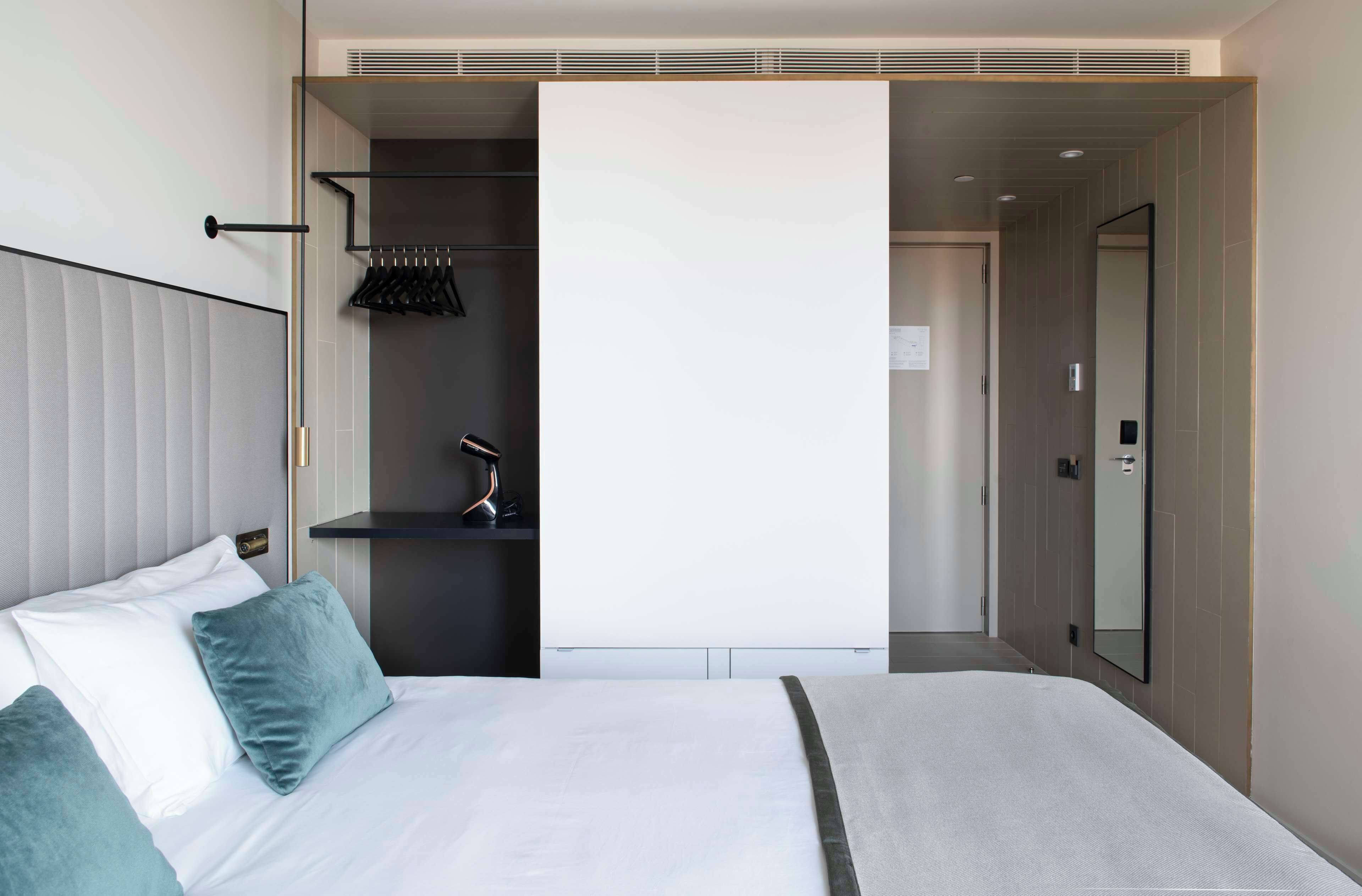 Habitación de hotel moderna con una cama grande, un armario, un espejo y una puerta que da a otra habitación.