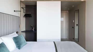 Habitación de hotel moderna con una cama grande, un armario, un espejo y una puerta que da a otra habitación.
