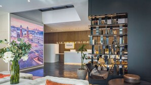 Un vestíbulo moderno con una gran pantalla digital mostrando un paisaje urbano, una recepción con la leyenda 'Occidental' y una estantería llena de libros.