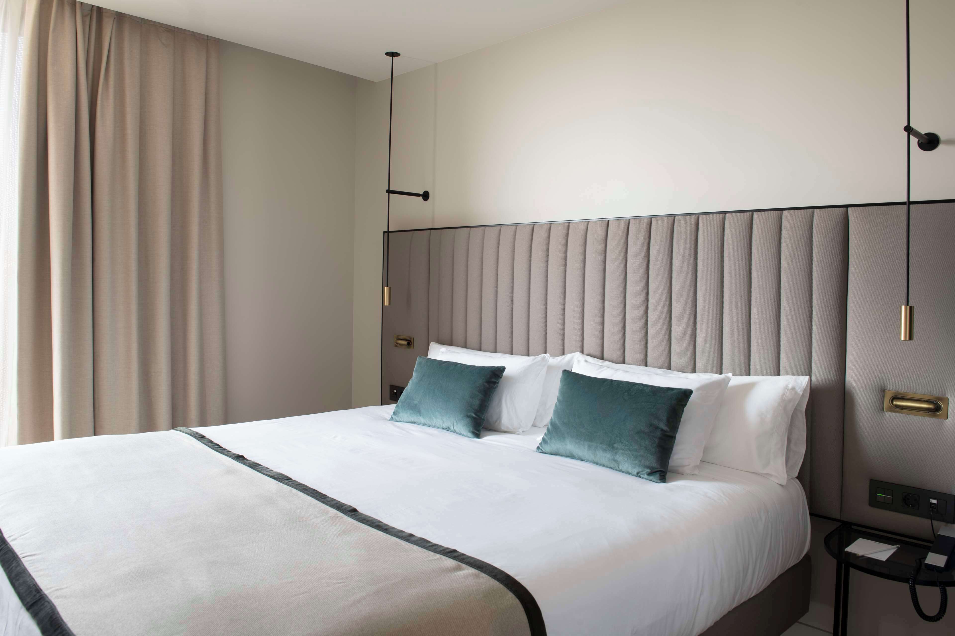A modern hotel room with a large bed, a nightstand, and a wall-mounted telephone.