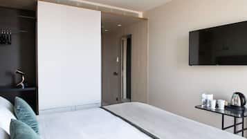 Quarto de hotel moderno com cama, televisão fixada na parede e uma mesinha com chaleira e chávenas.