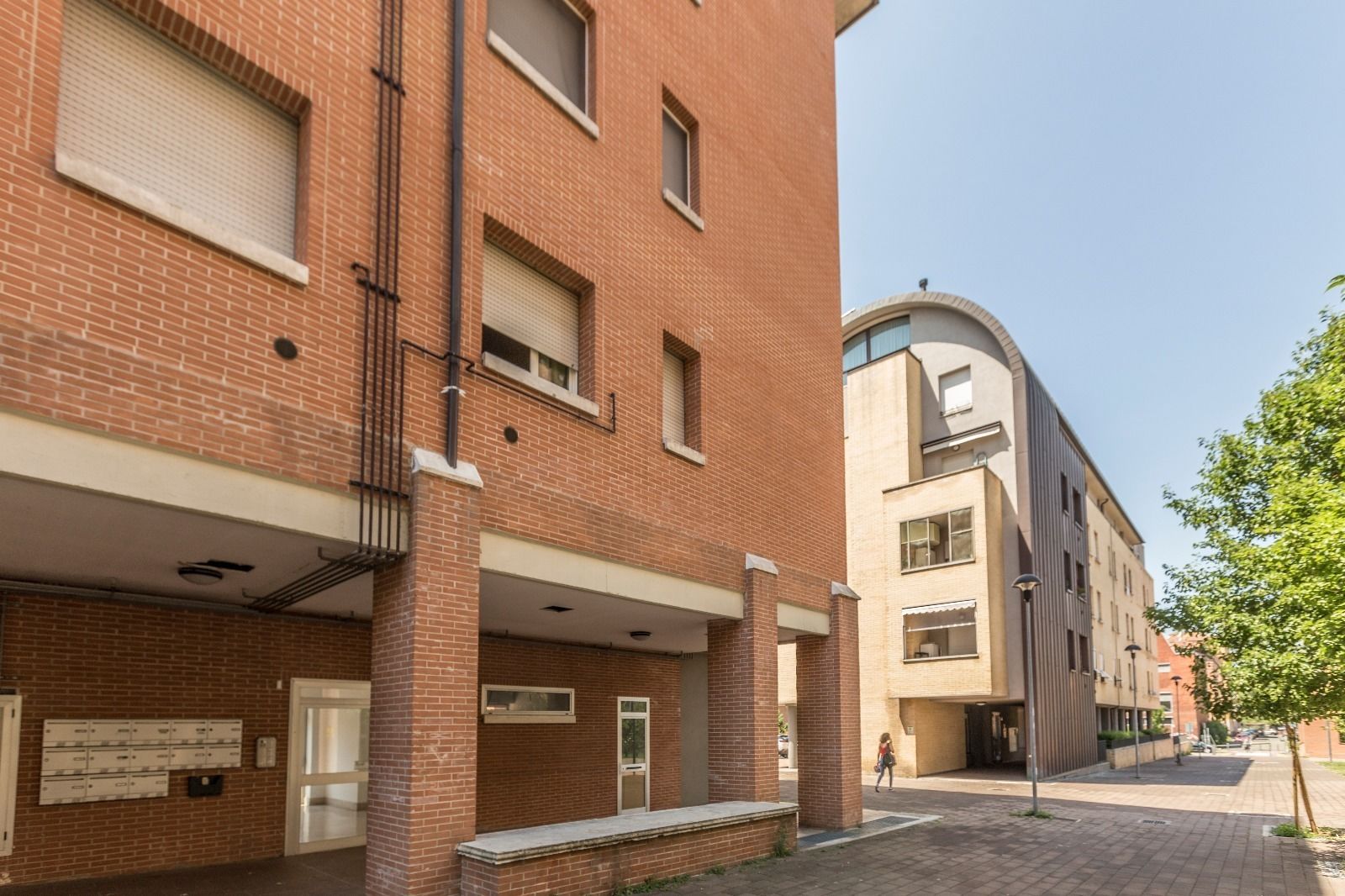 Un immeuble à plusieurs étages, doté d’une façade en briques, de grandes fenêtres et d’un espace extérieur couvert avec des bancs.
