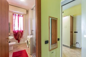 A bathroom with a toilet, washing machine, and a shower area.