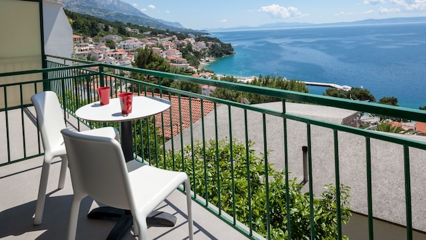 A balcony with a table and chairs, overlooking a coastal town and the sea. - Apartment Juric (Brela)