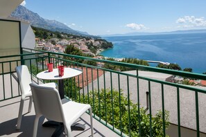 Un balcone con tavolo e sedie, affacciato su una cittadina costiera e il mare.