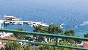 A marina with boats docked, a jet ski in the water, and a view of the surrounding area including trees and buildings. - Apartment Juric (Brela)