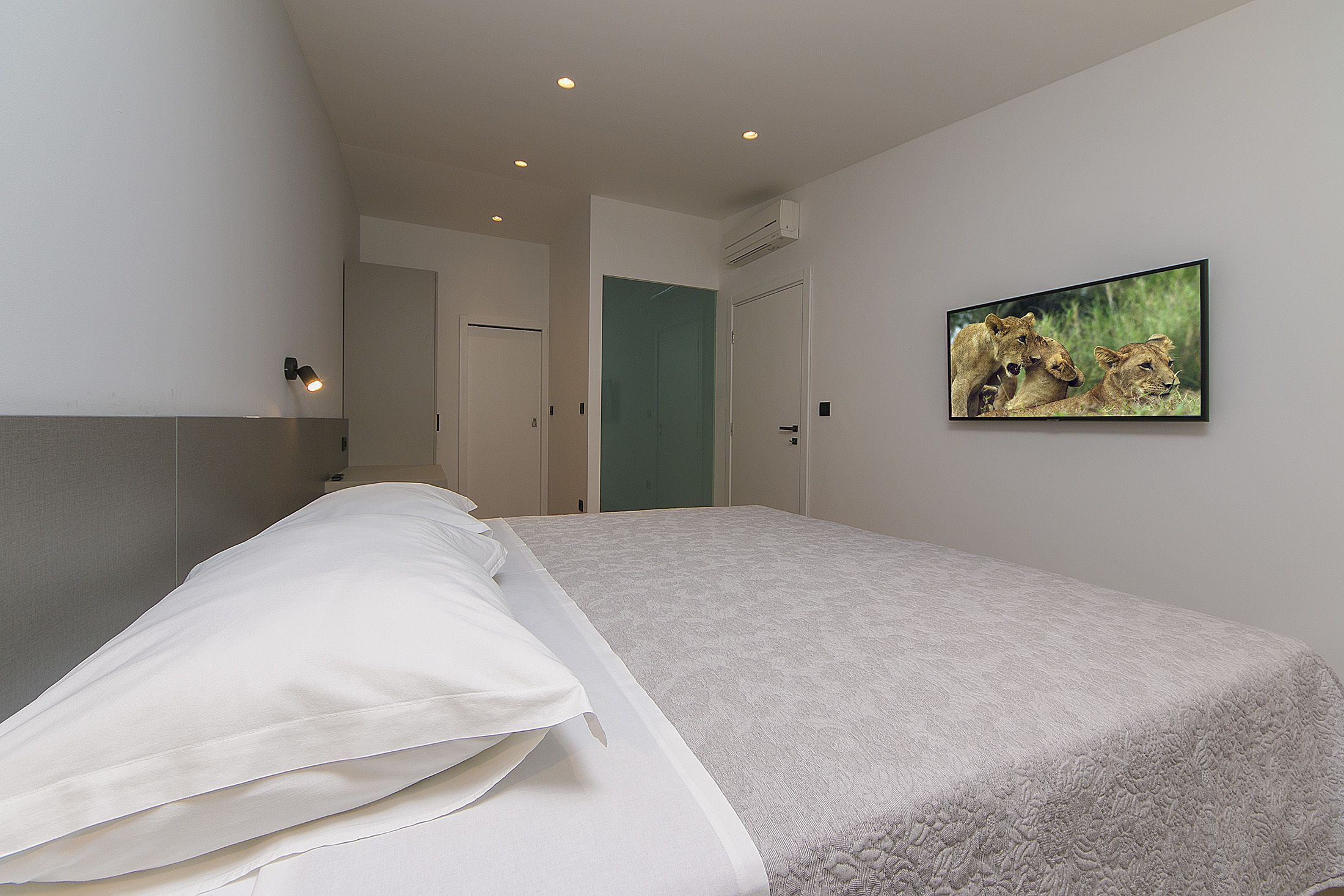 A bedroom with a bed, a wall-mounted TV, and a door leading to another room.