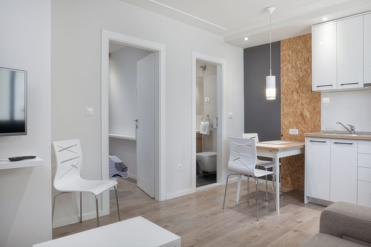 A modern kitchen with white cabinets, a wooden accent wall, and a dining area with white chairs.