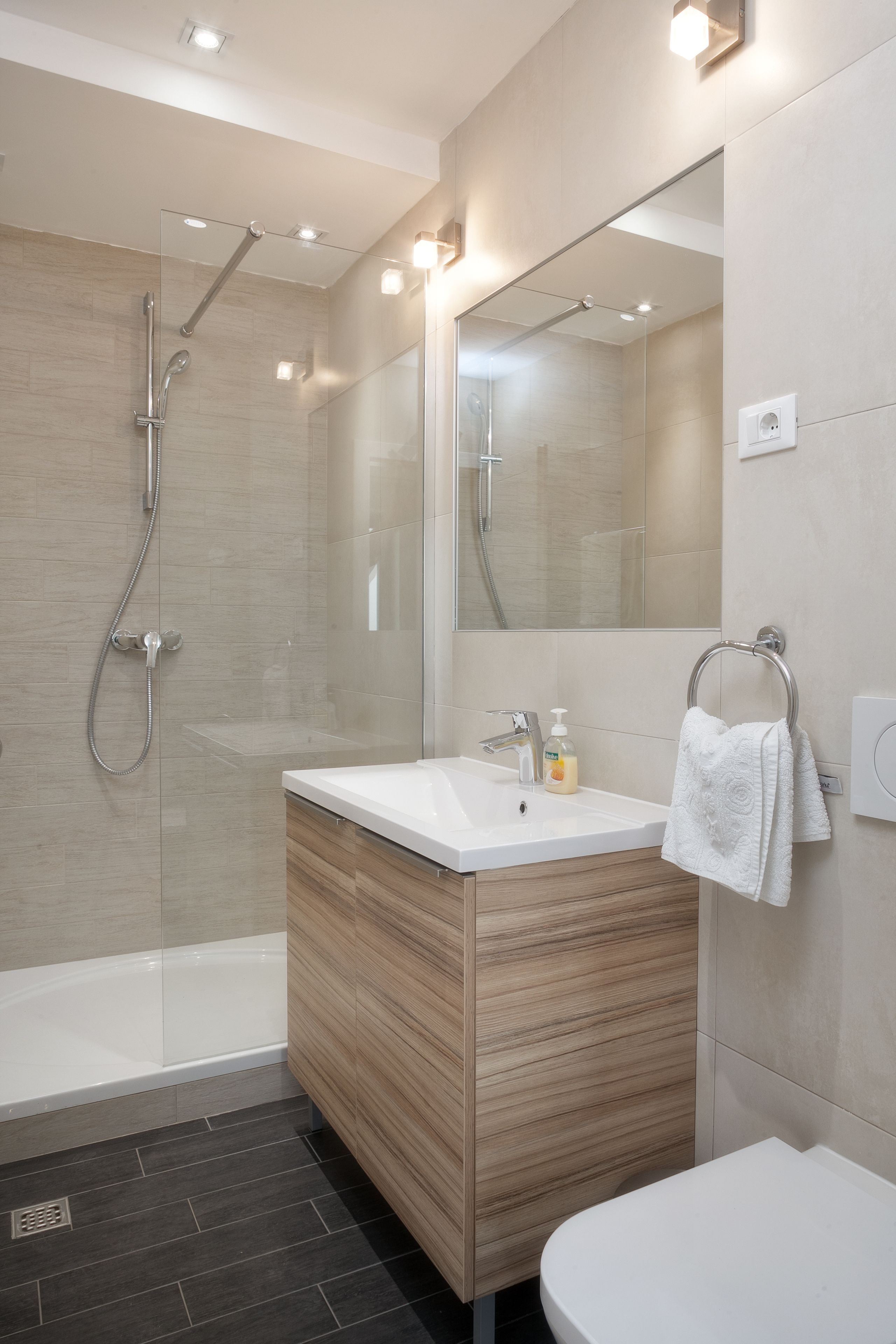 A modern bathroom with a glass-enclosed shower, a wooden vanity, a white sink, and a large mirror.