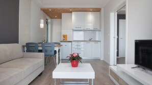 A modern living room with a sofa, a dining table with chairs, a white coffee table with a red vase, and a kitchen in the background. - Apartment Juric (Brela)