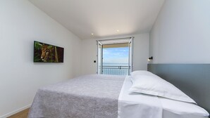 A bedroom with a bed, a painting, and a view of the sea through an open door. - Apartment Juric (Brela)