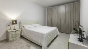 Ein Schlafzimmer mit einem Bett, Nachttisch, Lampe und Schreibtisch mit Computer und Pflanzen.